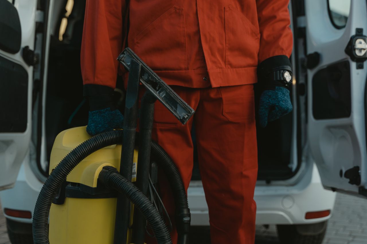 services-02 A professional cleaner in a red uniform holding a vacuum near a van, ready for service.